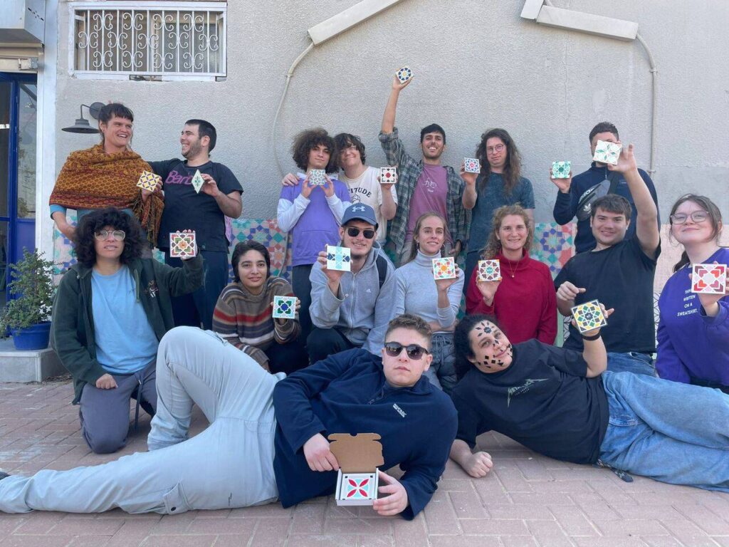 קבוצה של אנשים מציגה אריחים צבעוניים עם דוגמאות גיאומטריות על רקע קיר.