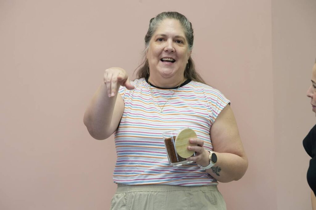 אישה עם חולצה מפוספסת מחזיקה מיכל זכוכית, מחייכת ומצביעה עם היד לצד.