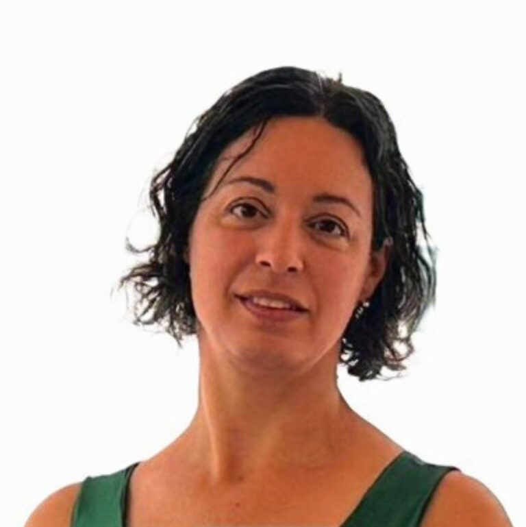 אישה עם שיער קצר וגלי בחולצה ירוקה, מביטה קדימה על רקע לבן.